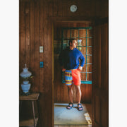 Man wearing navy sweatshirt and Canoe stripe lounge short standing inside looking out the window.
