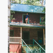 Man wearing navy sweatshirt and Canoe stripe lounge short leaning out window on roof.