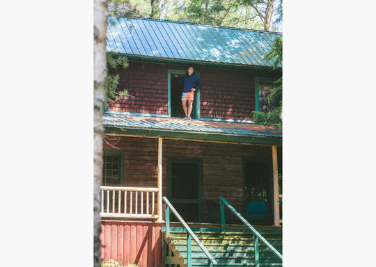 Man wearing navy sweatshirt and Canoe stripe lounge short leaning out window on roof.