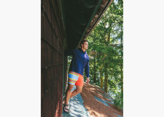 Man wearing navy sweatshirt and Canoe stripe lounge short leaning out window on roof.