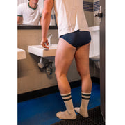 Man standing in bathroom in front of sink wearing blue boxers and black stripe classic crew socks.