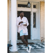 Man standing in front of house doorway holding a bowl wearing color block blues slim fit boxers and light pink dress shirt.