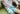Close up of man laying inside wearing white dress shirt and Light Blue Doghouse slim fit boxer (orange with small icons like dog house, golf clubs, card etc)