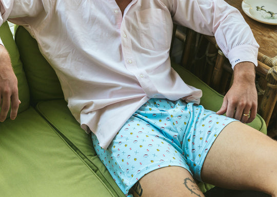 Close up of man laying inside wearing white dress shirt and Light Blue Doghouse slim fit boxer (orange with small icons like dog house, golf clubs, card etc)