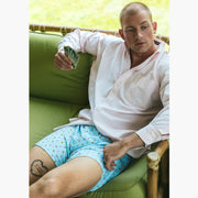 Man sitting  inside wearing white dress shirt and Light Blue Doghouse slim fit boxer (orange with small icons like dog house, golf clubs, card etc) holding some playing cards