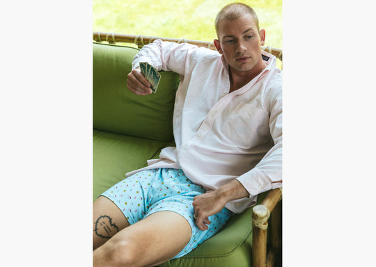 Man sitting  inside wearing white dress shirt and Light Blue Doghouse slim fit boxer (orange with small icons like dog house, golf clubs, card etc) holding some playing cards