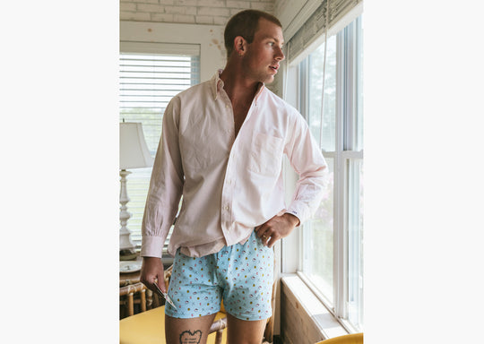 Man standing inside wearing white dress shirt and Light Blue Doghouse slim fit boxer (orange with small icons like dog house, golf clubs, card etc)