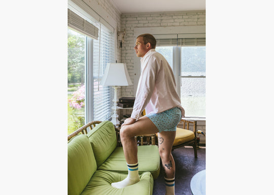 Man standing inside wearing white dress shirt and Light Blue Doghouse slim fit boxer (orange with small icons like dog house, golf clubs, card etc)