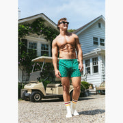 Shirtless man standing in front of a golf cart wearing a green Doghouse slim fit boxer (green with small icons like dog house, golf clubs, card etc)
