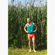 Man standing outside wearing green sleeveless top and orange Doghouse slim fit boxer (orange with small icons like dog house, golf clubs, card etc)
