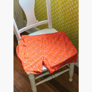 Oorange Doghouse slim fit boxer (orange with small icons like dog house, golf clubs, card etc) sitting on a white wooden chair.