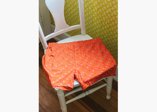 Oorange Doghouse slim fit boxer (orange with small icons like dog house, golf clubs, card etc) sitting on a white wooden chair.