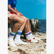 Close up side shot of two men sitting on wood pier at the beach wearing fieldhouse striped crew socks and red lounge shorts.