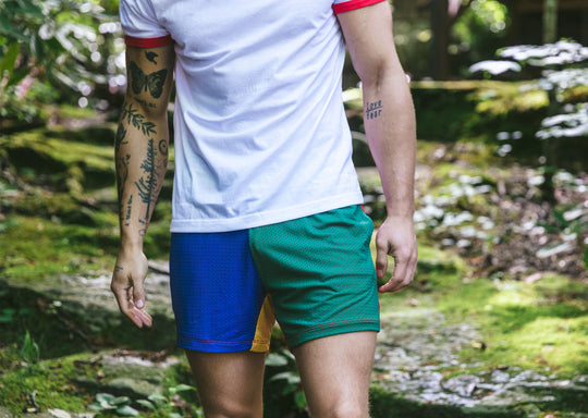 Close up of a man in forest wearing white t-shirt and blue/green/yellow multi colored mesh lounge shorts.