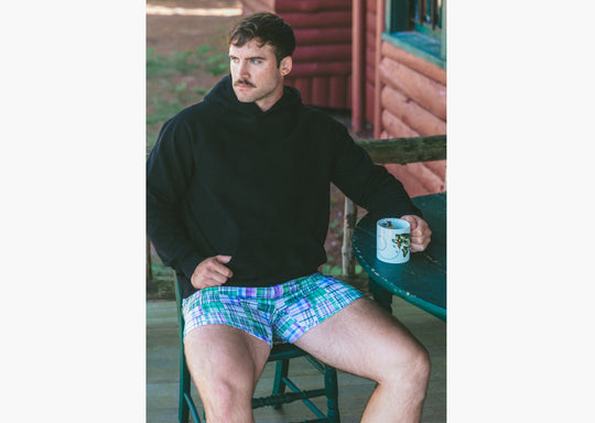 Man holding coffee sitting at table wearing black hoodie and green madras slim fit boxer