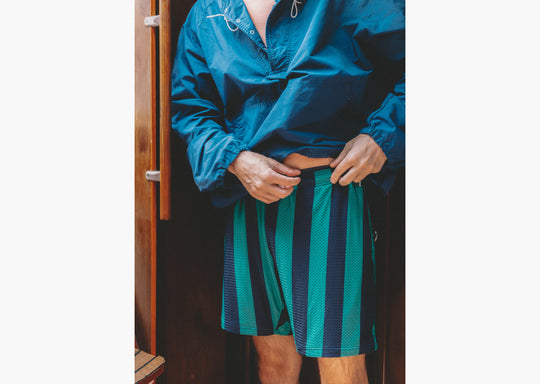 Close up shot of man on boat wearing green/navy lounge shorts and blue jacket