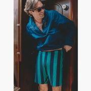 man on boat wearing green/navy lounge shorts and blue jacket