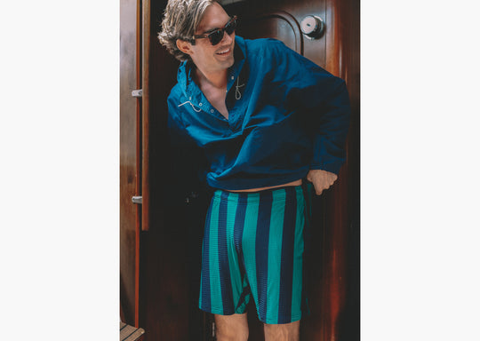 man on boat wearing green/navy lounge shorts and blue jacket