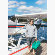 Man wearing grey hoodie standing on dock in front of small plane 