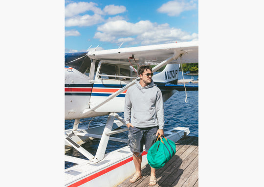 Man wearing grey hoodie standing on dock in front of small plane 