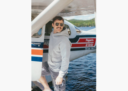 Man wearing grey hoodie standing on dock getting into a small plane 
