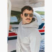 Close up of man wearing grey hoodie standing on dock in front of small plane 