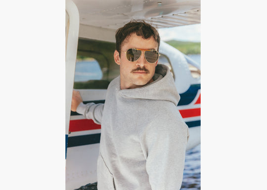 Close up of man wearing grey hoodie standing on dock in front of small plane 