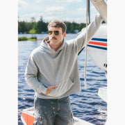 Man wearing grey hoodie standing on dock in front of small plane 