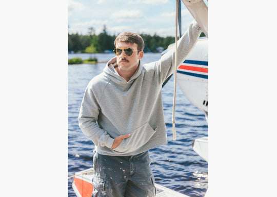 Man wearing grey hoodie standing on dock in front of small plane 