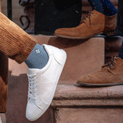 White sneakers and blue socks worn by a person sitting on steps with another person wearing brown shoes.