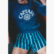 Close up of man sitting on boat holding radio wearing navy sweatshirt and navy stripe slim fit boxers.