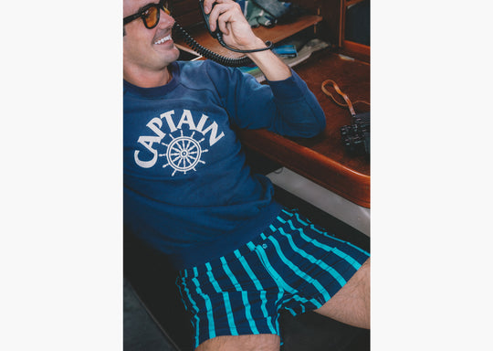 Man sitting on boat holding radio wearing navy sweatshirt and navy stripe slim fit boxers.