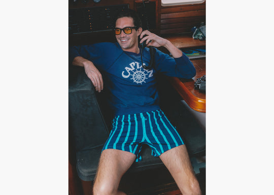 Man sitting on boat holding radio wearing navy sweatshirt and navy stripe slim fit boxers.