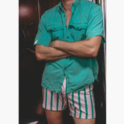 Man with arms crossed wearing light green collar shirt and pink/green stripe slim fit boxers.
