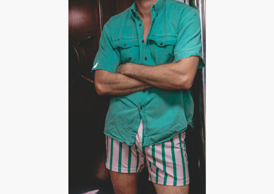 Man with arms crossed wearing light green collar shirt and pink/green stripe slim fit boxers.