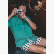 Man holding camera green collar shirt and pink/green stripe slim fit boxers.