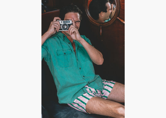 Man holding camera green collar shirt and pink/green stripe slim fit boxers.