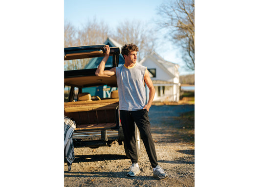 Man standing in front of car wearing sleeveless grey shirt and black lounge pants.