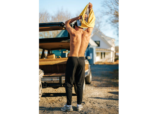 Man taking off shirt in front of car wearing black lounge pants.