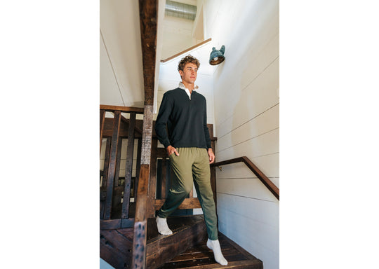 Man walking down stairs wearing a black sweater and olive lounge pants.