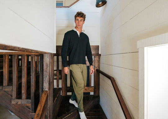 Man walking down stairs wearing a black sweater and olive lounge pants.