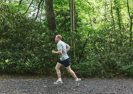 Man running in a forest wearing grey tshirt and navy blue lounge shorts.