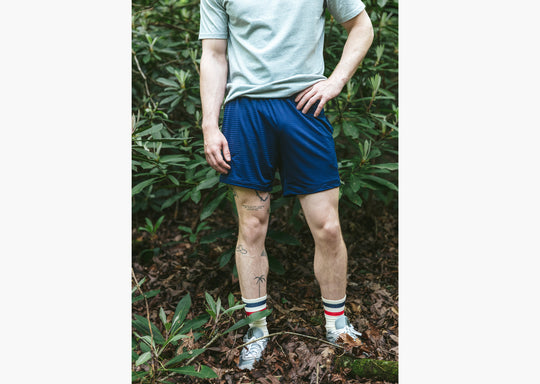 Close up shot of man standing in forest with hand on hip wearing grey tshirt and navy blue lounge shorts.