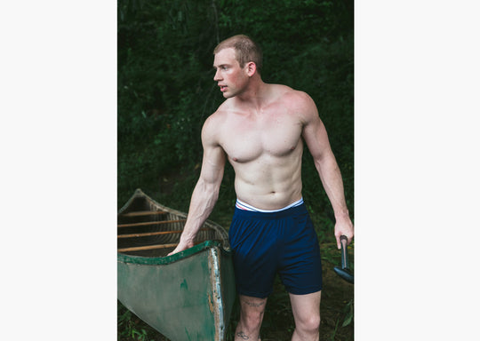 Shirtless man in forest pulling a canoe wearing navy blue lounge shorts.