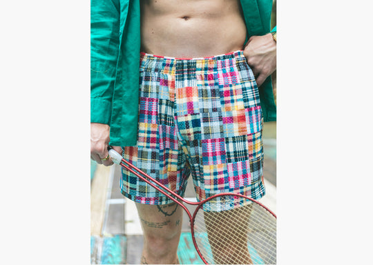 Close up shot of man wearing Madras print lounge short, opened green dress shirt, and holding a racket.