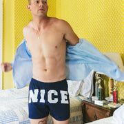 Man in "NICE" slim fit boxers in bedroom with yellow wallpaper.
