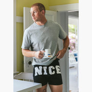 Man in kitchen holding coffee mug and wearing a pair of black slim fit boxers with the words "NICE" in big bold white font.