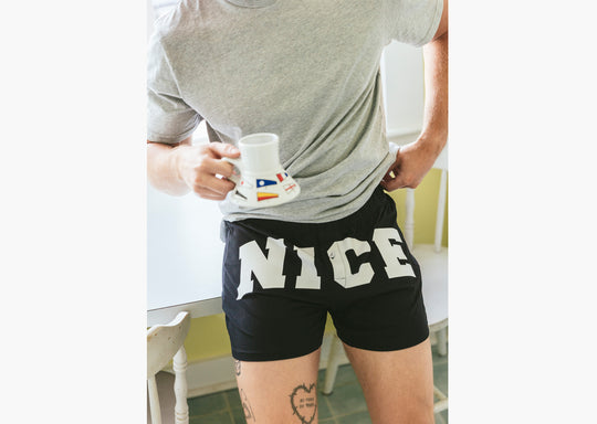 Close up of man in kitchen holding coffee mug and wearing a pair of black slim fit boxers with the words "NICE" in big bold white font.