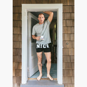 Man in doorway holding coffee mug and wearing a pair of black slim fit boxers with the words "NICE" in big bold white font.