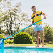 Man standing outside by pool wearing yellow polo and grey slim fit boxers with words "NICE" on the front in white bold font.